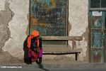 Tajik woman sitting on a bench in front of a shuttered window in Tashkurgan