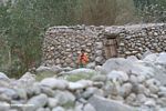 Tajik boy in an orange jacket standing in front of his stone home
