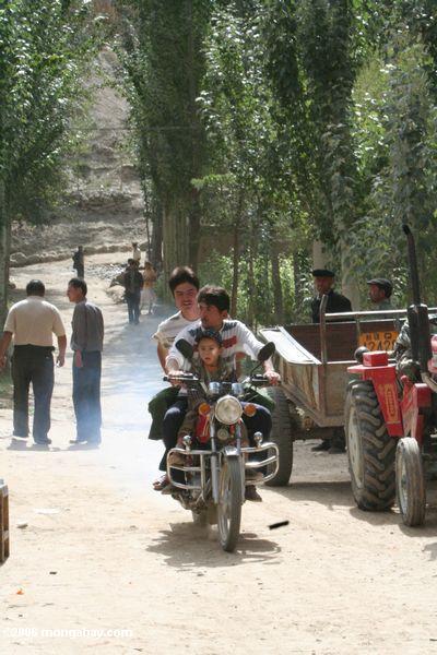 Junge und sein Vater, die ein Motorradreiten hinunter die Hauptstraße im Datong Dorf Xinjiang