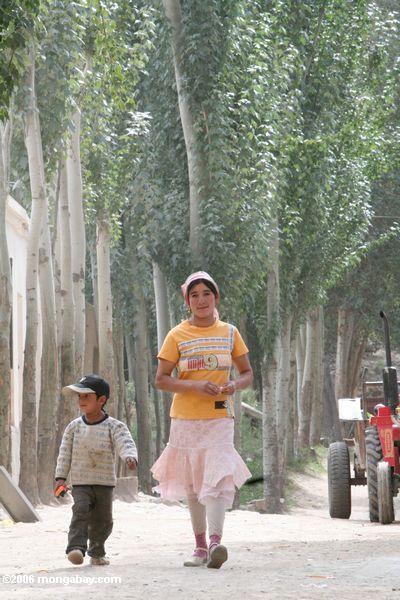 Mädchen, das mit ihrem Bruder hinunter die Hauptstraße im Datong Dorf Xinjiang
