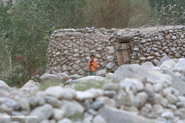 Tajik Junge in einer orange Jacke, die vor seinem SteinhauptXinjiang